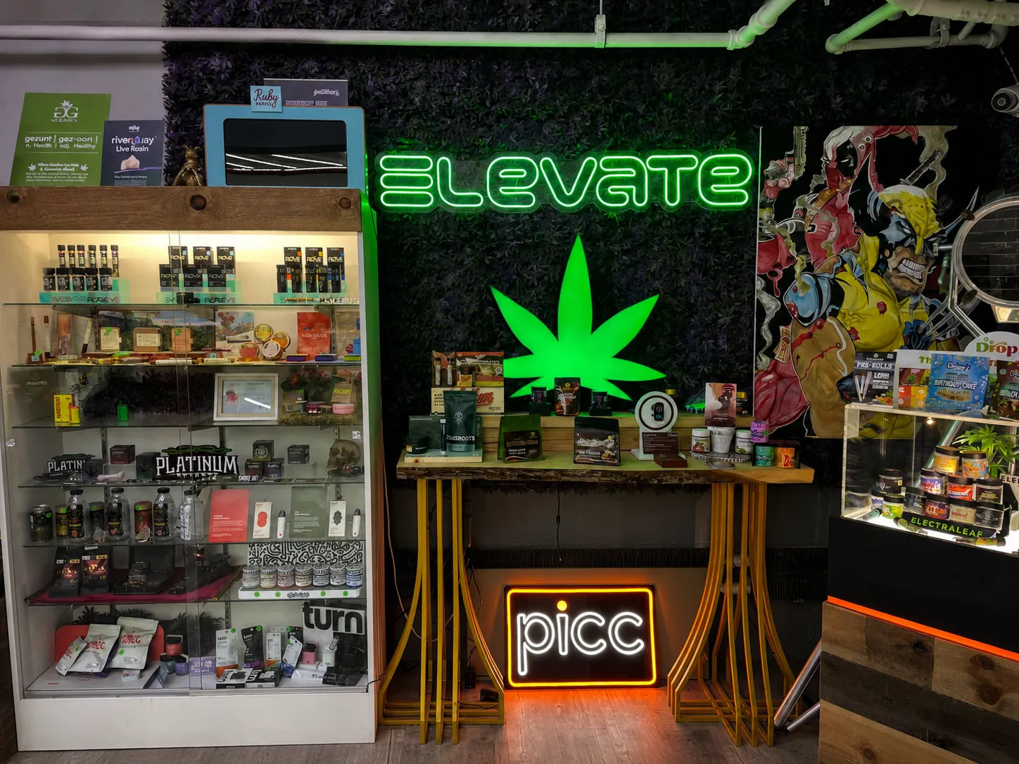 Green neon Elevate sign and glowing cannabis leaf above a product display table